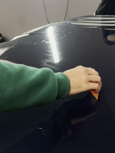 Installer squeegeeing paint protection film onto a hood